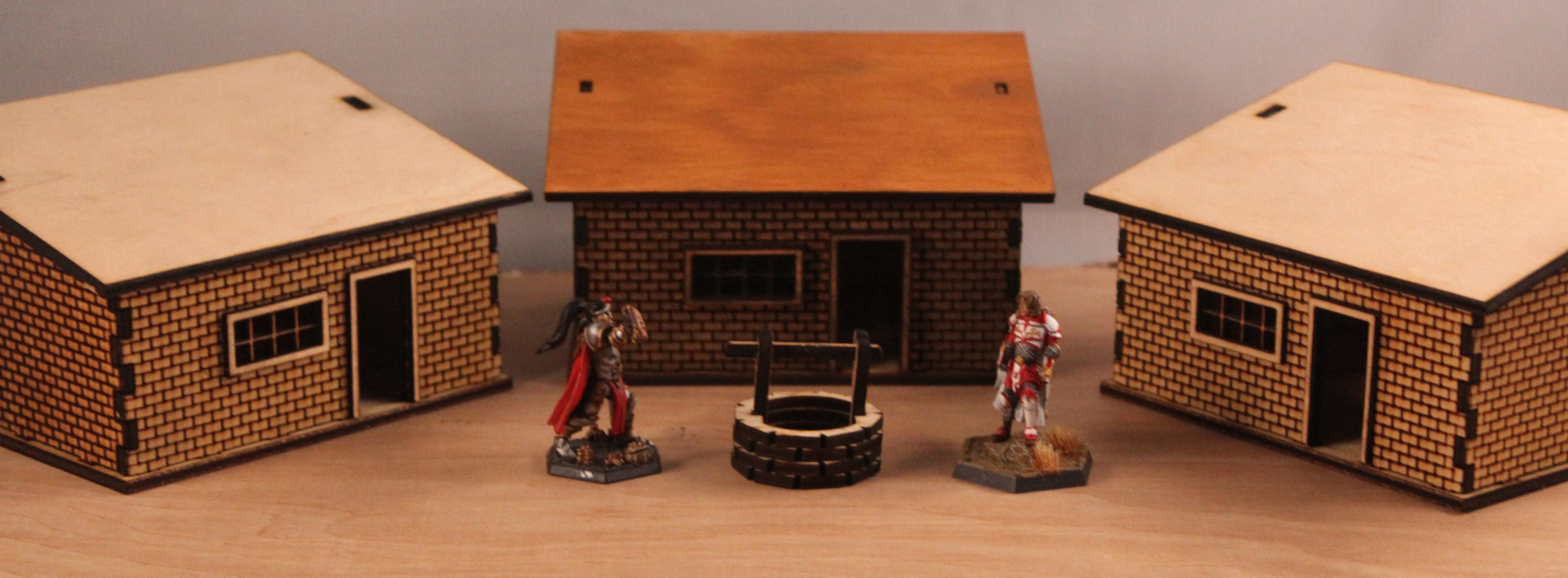 Two small miniature figurines standing near a well with three legacy slant houses behind them.